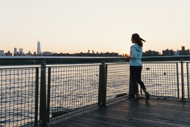 Mid adult woman gazing at sunset on city waterfront at dusk