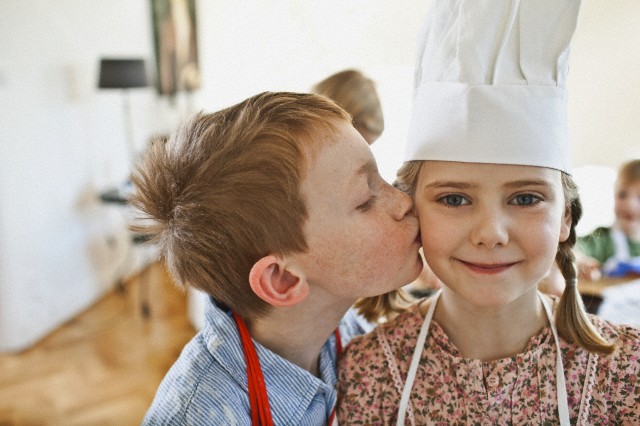 Close up of boy (5-6) kissing girl (5-6) wearing chef's hat