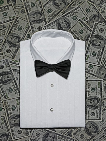 Elegant white shirt with bow tie on background made of dollar banknotes, studio shot