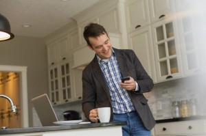 Man checking cell phone as he has coffee in the kitchen.